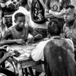 Black and white street photography of a group of men playing dominoes on a street in Havana, Cuba, capturing intense focus and social tradition